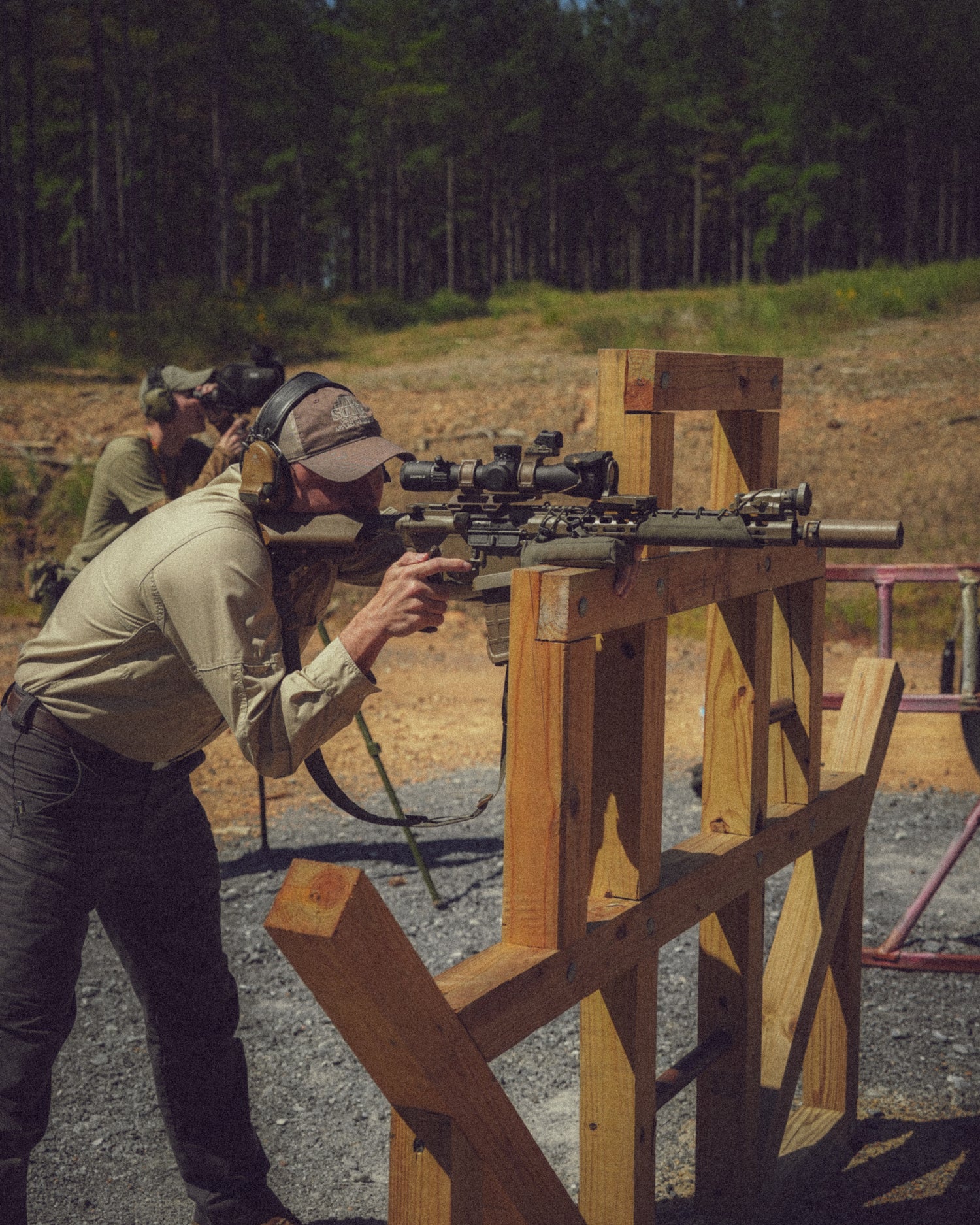 Two people at a shooting range with rifles, one person is aiming.