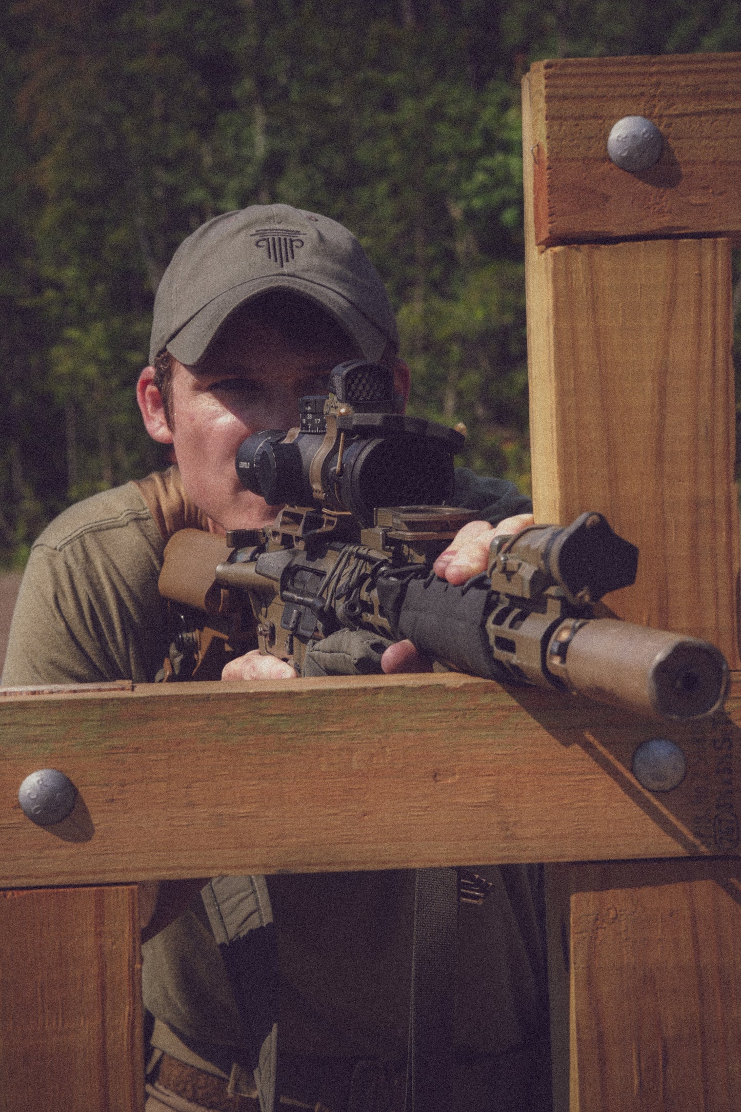 Person aiming a rifle through a scope in a wooded area