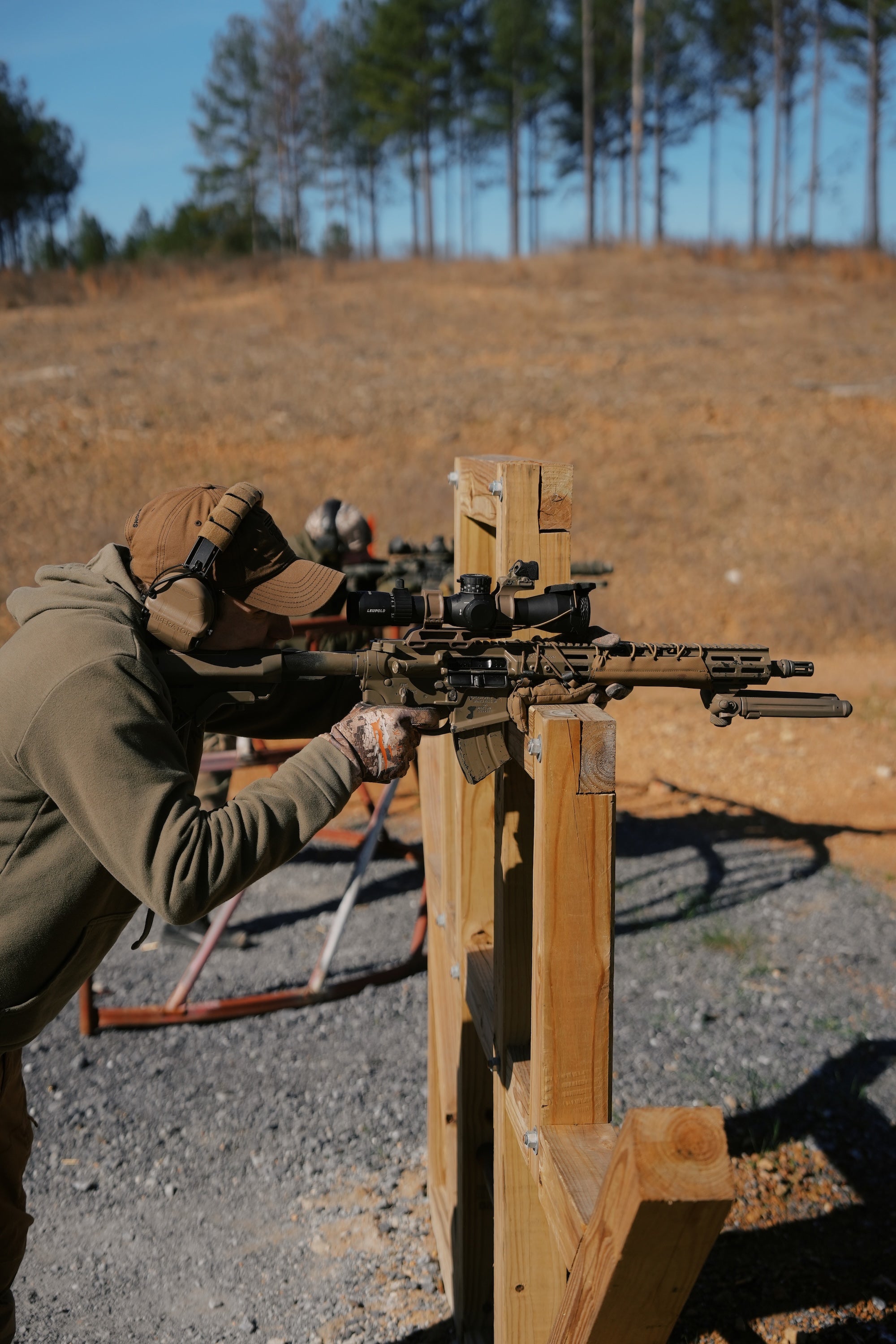 Person aiming a rifle at a target with trees in the background